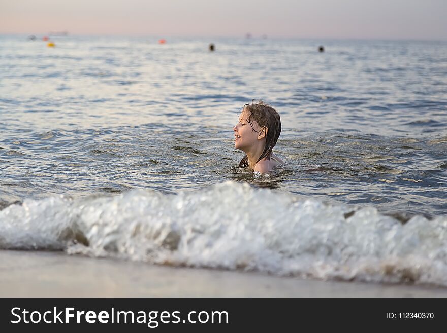 Seven-year-old girl bathes the sea waves in the rays of the sunset. Seven-year-old girl bathes the sea waves in the rays of the sunset