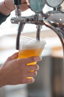 Plastic Cup Of Beer Flowing From Beer Tap With Nice Foam Close-up In Female Bartender Hands Royalty Free Stock Images
