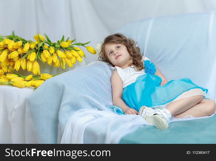 Beautiful little girl sitting on the sofa with a bouquet of yellow tulips. Beautiful little girl sitting on the sofa with a bouquet of yellow tulips.