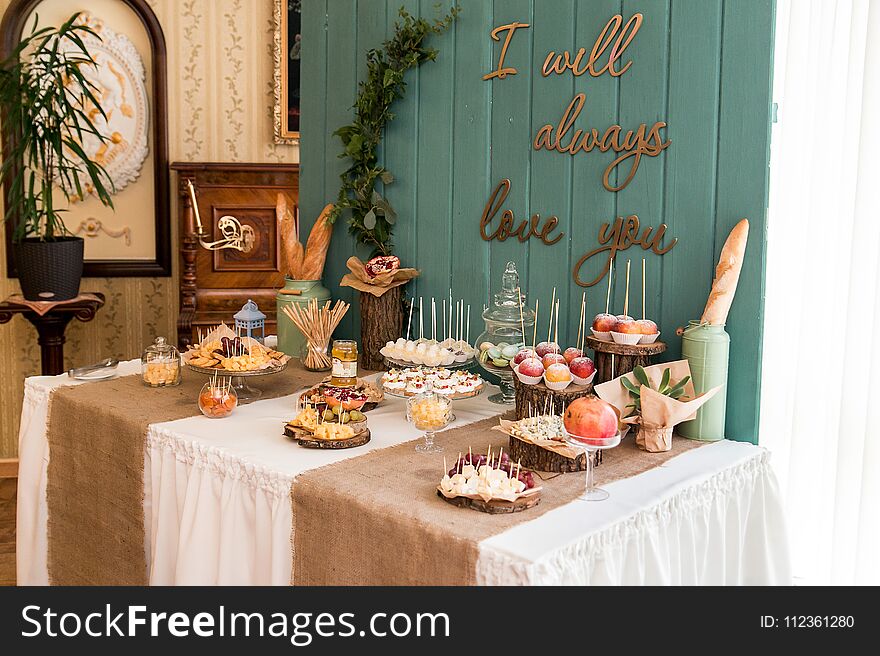 A rustic table, sealed with cheese, nuts, fruits and sweets. A wooden background.