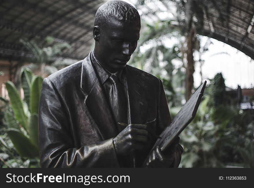 Man Wearing Blazer Holding Book and Pen Statue