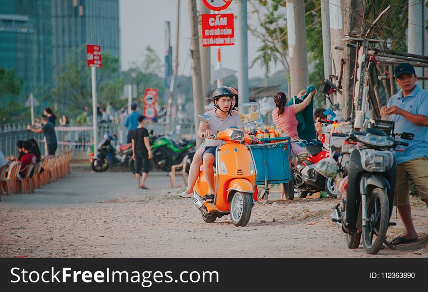 Man Wearing Grey Shirt Riding on Orange Motor Scooter at Daytime