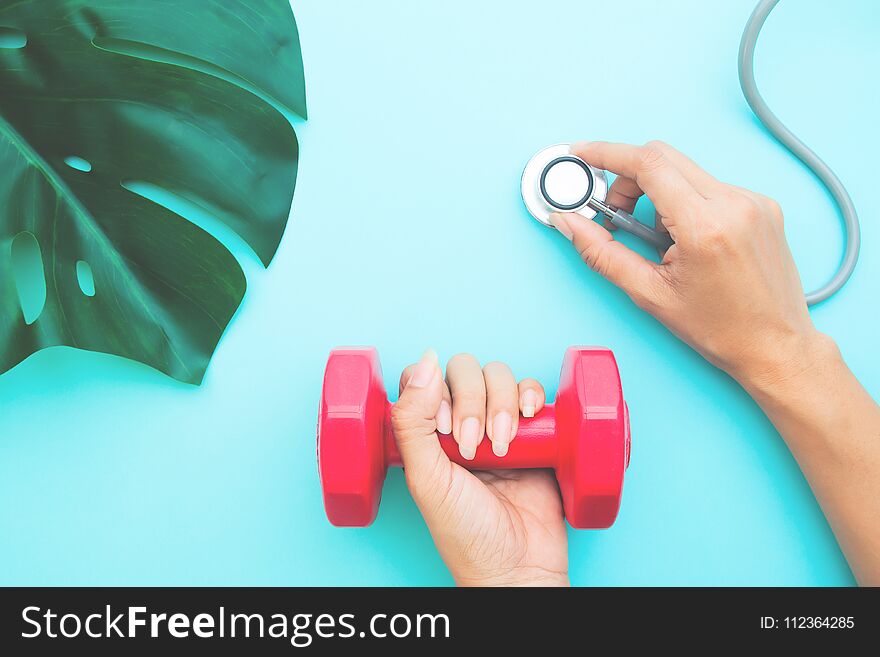 Healthcare and Diet concept, Doctor`s hands holding stethoscope and dumbbell on blue pastel background