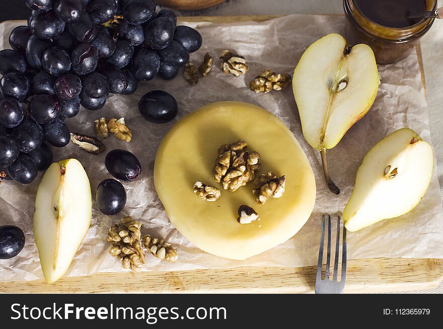Cheese, honey, grapes, pears and nuts on wooden board on kitchen