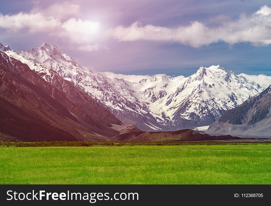 Beautiful landscape of mountain ranges and green grass meadow field under white clouds in the blue sky in sunny summer day. Shot in Mt Cook, the highest mountain in New Zealand. Beautiful landscape of mountain ranges and green grass meadow field under white clouds in the blue sky in sunny summer day. Shot in Mt Cook, the highest mountain in New Zealand.