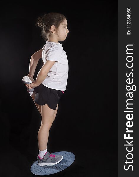 Little caucasian girl in on one leg position staing on balance board. Photo on black background. Little caucasian girl in on one leg position staing on balance board. Photo on black background