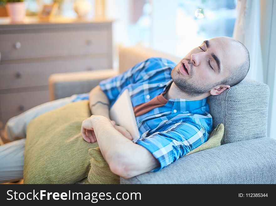 Young man sleeping on sofa with laptop