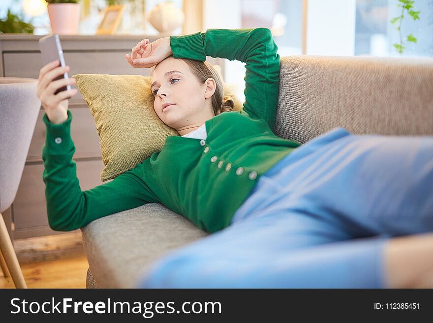 Woman browsing internet on her smartphone lying on the sofa at home. Woman browsing internet on her smartphone lying on the sofa at home