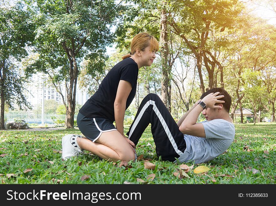 Asian Sweet Couple Exercising Together With Smile On Their Faces On Soft Grass Encircle With Nature And Warm Light From The Sun.