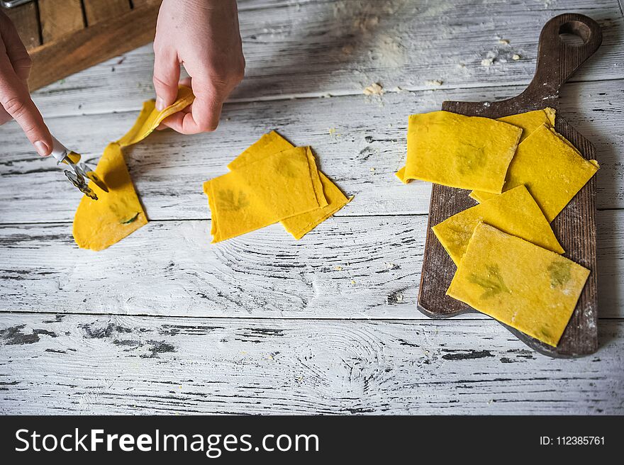 These multicolored pasta recipes are dyed with organic vegetables and spices on a wooden background. Preparation of yellow lasagna at home with parsley and basil, male hands cut pasta on a white wooden table