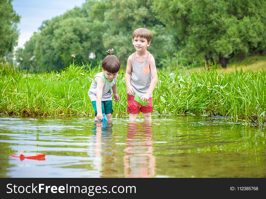 Two little brothers playing with paper boats by a river on warm