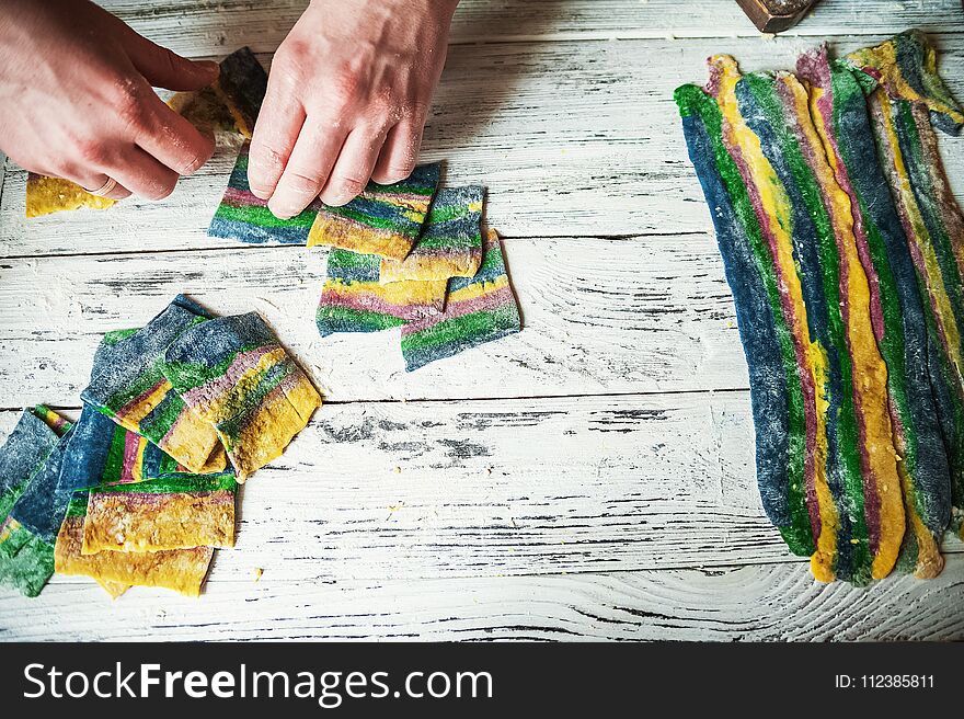 These multicolored pasta recipes are dyed with organic vegetables and spices on a wooden background. Preparation of yellow lasagna at home with parsley and basil, male hands cut pasta on a white wooden table