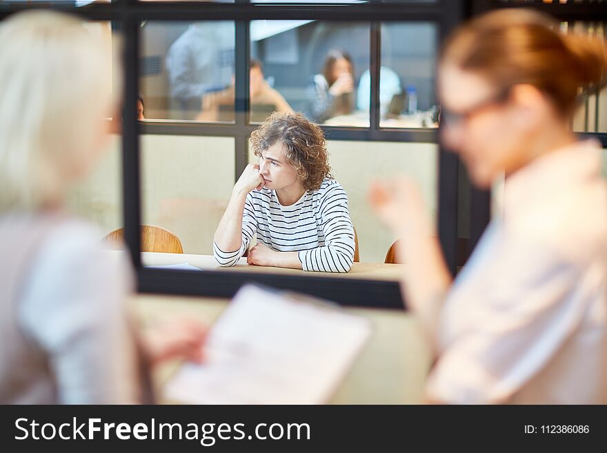 Upset young men sitting by desk in boardroom and being nervous about decision of employers after interview. Upset young men sitting by desk in boardroom and being nervous about decision of employers after interview