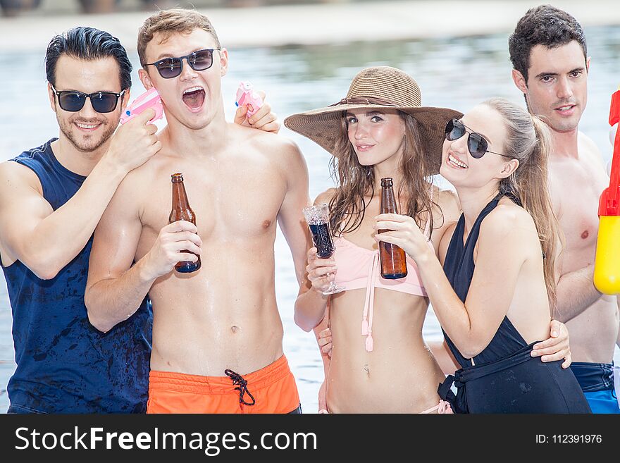 Group of friends making party in the pool and Drinking beverage with water gun