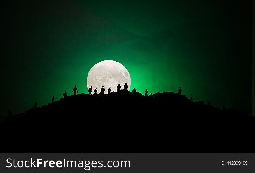 Scary view crowd of zombies on hill with spooky cloudy sky with fog and rising full moon. Silhouette group of zombie walking under