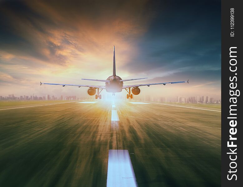 Air plane flying over airport runway with city scape and sunset