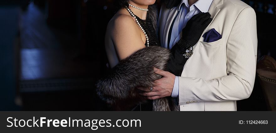 Man in white classic suit hugging woman in evening black dress and fur cape. Man in white classic suit hugging woman in evening black dress and fur cape