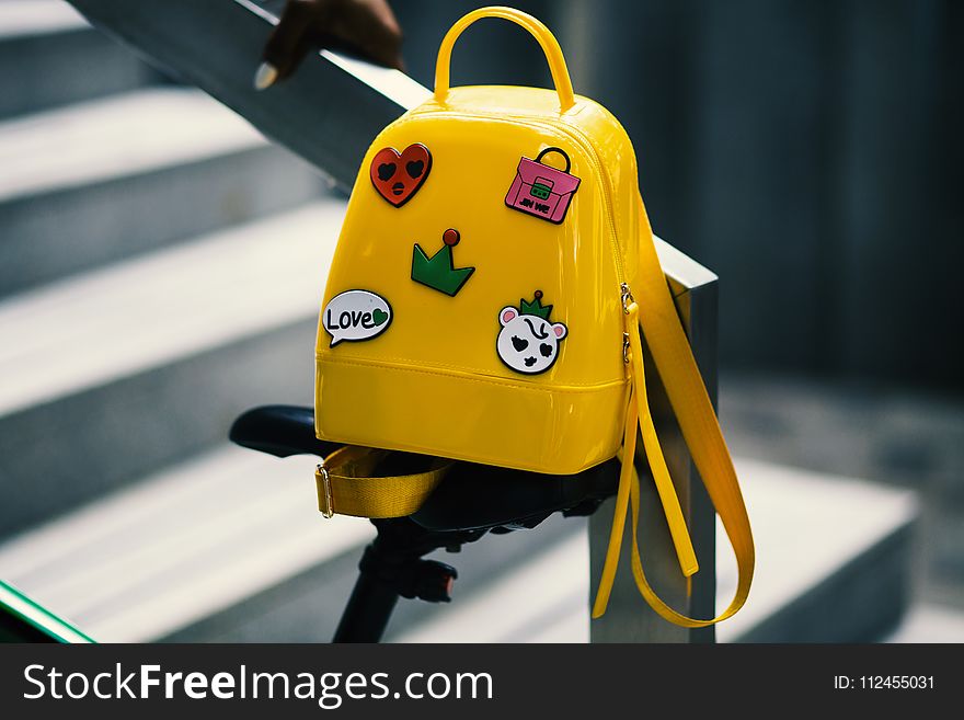 Yellow Backpack With Five Assorted Stickers on Grey Metal Stairway Rail