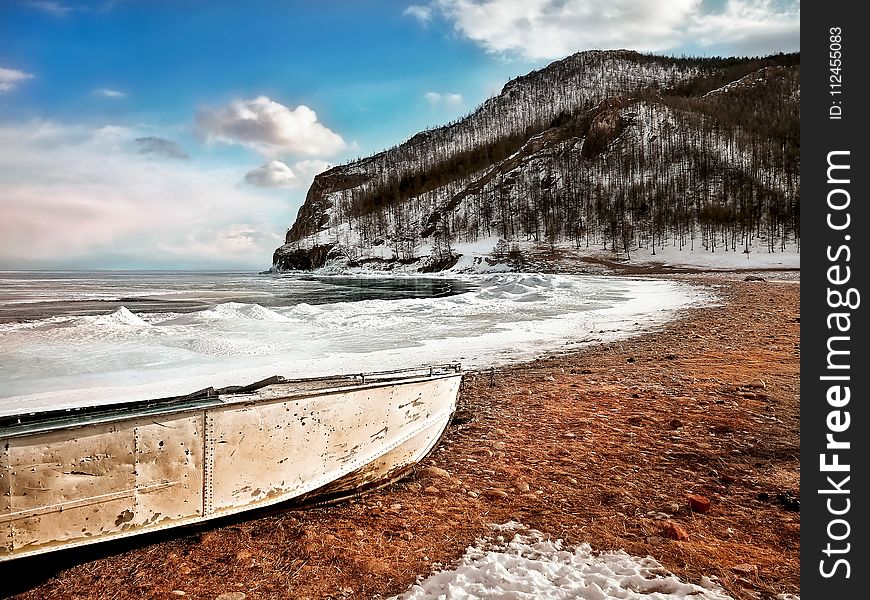 White Boat On Seashore Near Mountain Under White And Blue Sky