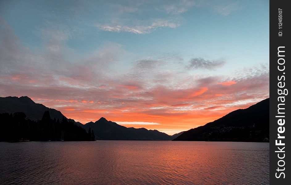 Body of Water Near Silhouette of Mountain Under White Clouds during Sunset