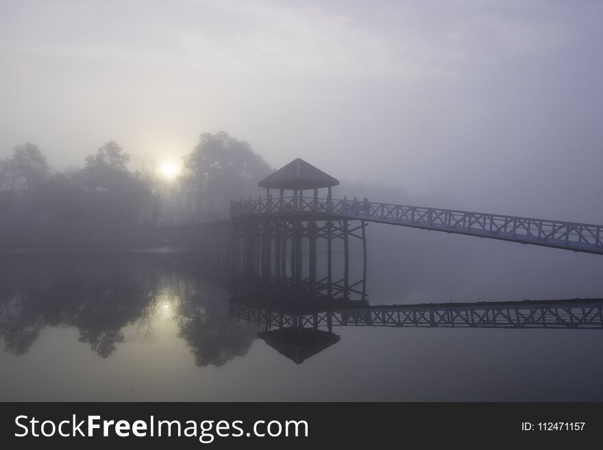 The only sound that of birdsong, as the sun penetrates through a blanket of fog casting a mirror reflection upon the water in the early morning on the Cape Fear River in Wilmington, North Carolina. The only sound that of birdsong, as the sun penetrates through a blanket of fog casting a mirror reflection upon the water in the early morning on the Cape Fear River in Wilmington, North Carolina