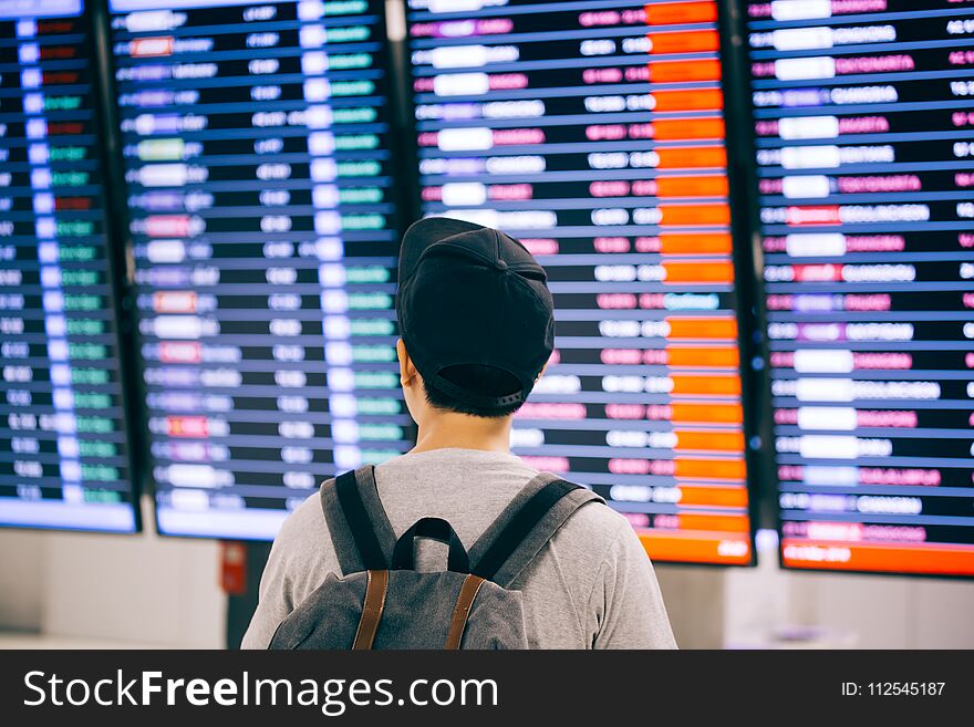 Young Male Traveler Watching And Waiting For Flight Time Schedule On Boarding Time Monitor Screen.