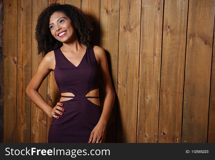 Woman in Purple V-neck Cutout Dress Leaning on Brown Wooden Wall