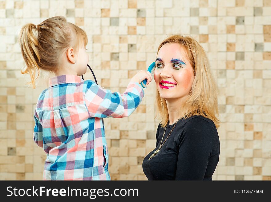 Cute little girl are doing funny make up to her mother.