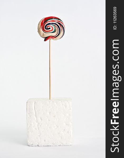 A colorful lollipop on white background supported on a polystyrene white cube. A colorful lollipop on white background supported on a polystyrene white cube