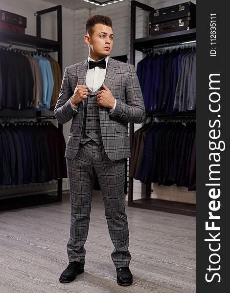 Sale, shopping, fashion, style and people concept - elegant young man choosing and trying jacket on in mall or clothing