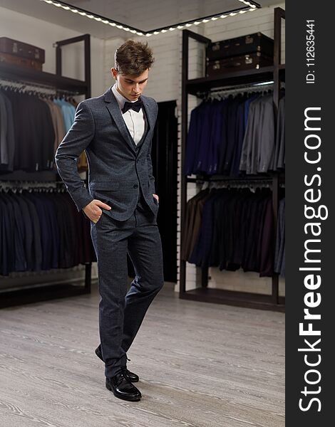 Businessman in classic vest against row of suits in shop. A young stylish man in a jacket. It is in the showroom, trying on clothes, posing. Advertising photo. Businessman in classic vest against row of suits in shop. A young stylish man in a jacket. It is in the showroom, trying on clothes, posing. Advertising photo