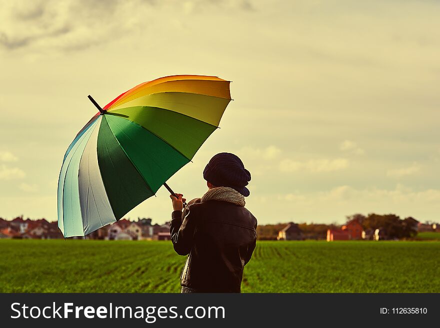 Boy on the field with a bright colorful umbrella .