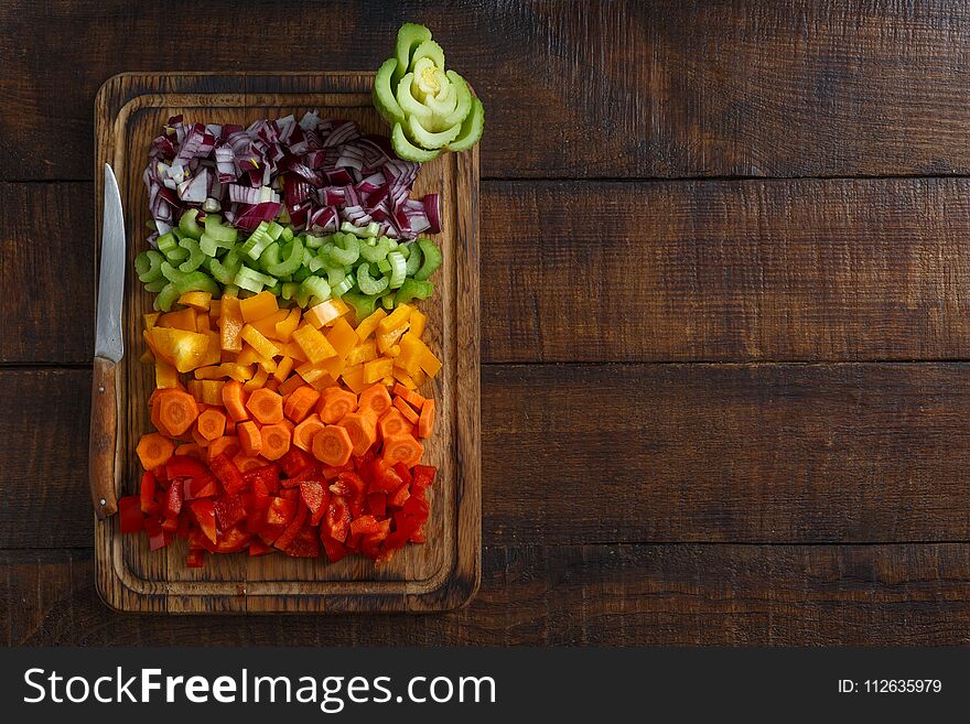 Chopped fresh vegetables arranged on cutting board on dark wooden table with border, top view. Chopped fresh vegetables arranged on cutting board on dark wooden table with border, top view