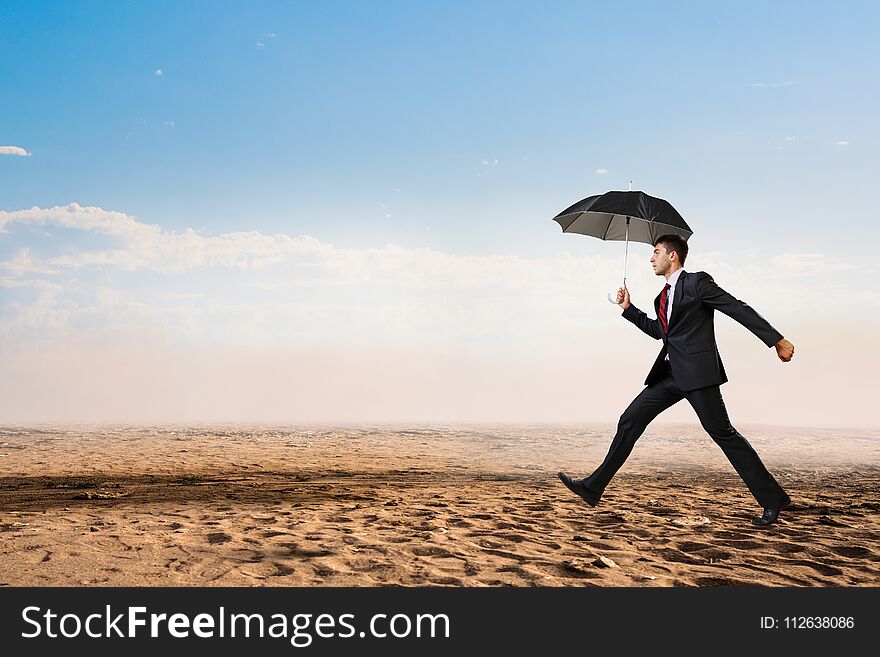 Businessman in suit with black umbrella running in desert. Mixed media. Businessman in suit with black umbrella running in desert. Mixed media