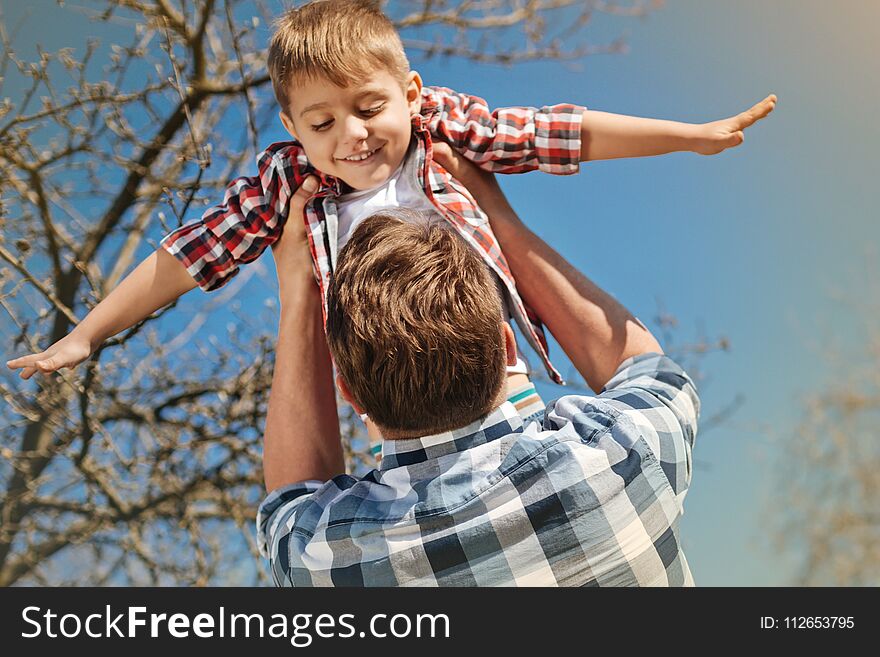 Just fly. Low angle of a positive nice boy in hands of his loving father spinning him outdoors. Just fly. Low angle of a positive nice boy in hands of his loving father spinning him outdoors