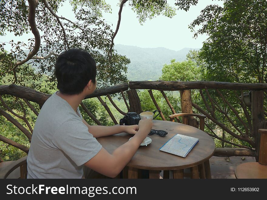 Relax time of happy young Asian man holding coffee cup and looking at beautiful nature .