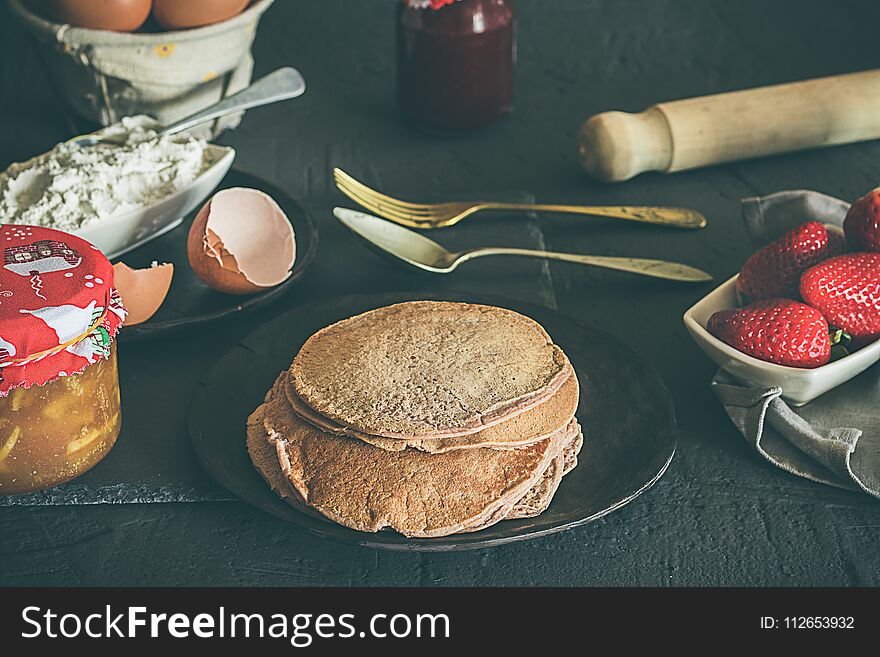 Ingredients for pancakes, jam, eggs, flour and strawberries. Dark rustic set