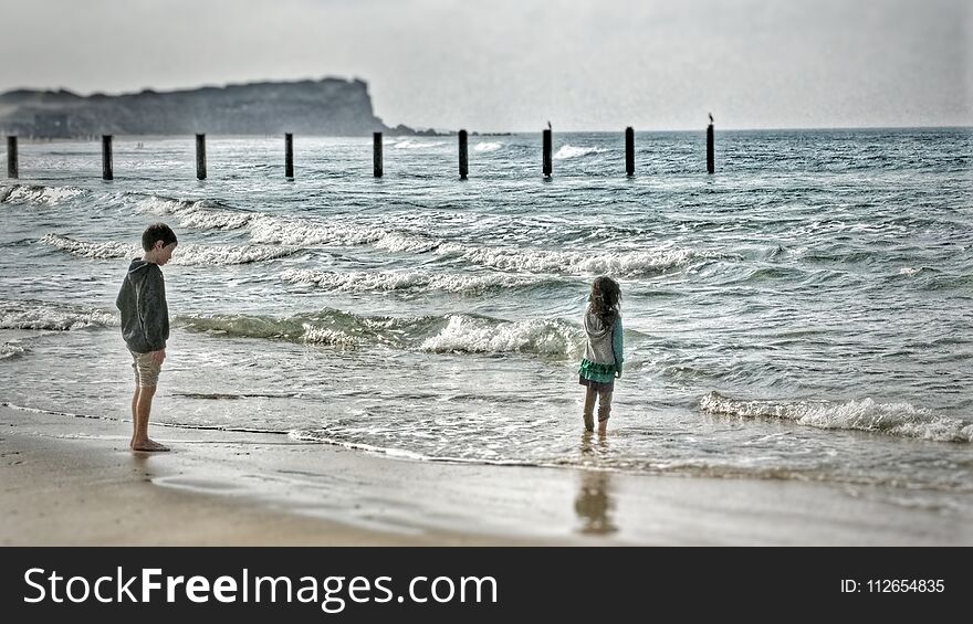 Two Young Children Standing On The Beach Watching The Waves