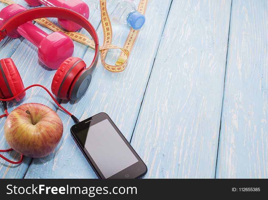 Fresh fruit with dumbbells on a wooden countertop, copy space, diet, and healthy food concept. Headphones and phone. Music in sport
