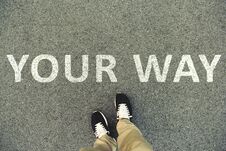 Words `Your Way` Written On An Asphalt Road. Top View Of The Legs And Shoes. POV Stock Photography