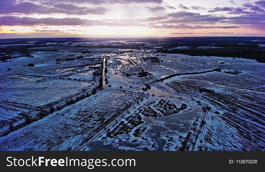 Violet sunset over a city with a horizon. Frozen water and meadows.