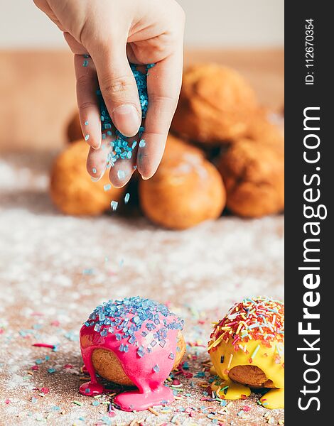 Woman`s hand sprinkling sugar strands on colorful doughnuts. Decoration. Woman`s hand sprinkling sugar strands on colorful doughnuts. Decoration.