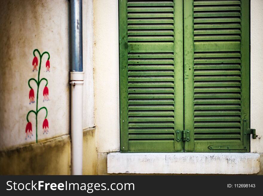 Closed window with green shutters and painted wall of old house