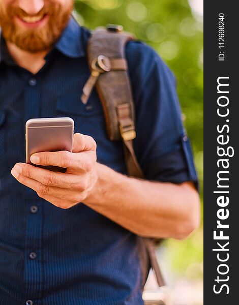 A happy handsome bearded male tourist in casual clothing using a phone.