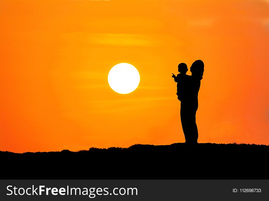 silhouette of a mother carrying her son watching the sunset