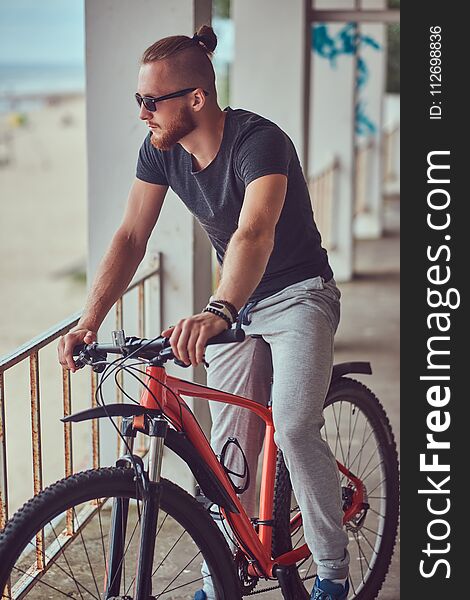 Handsome redhead male with a stylish haircut and beard dressed in sportswear with a bicycle standing outside. Handsome redhead male with a stylish haircut and beard dressed in sportswear with a bicycle standing outside.