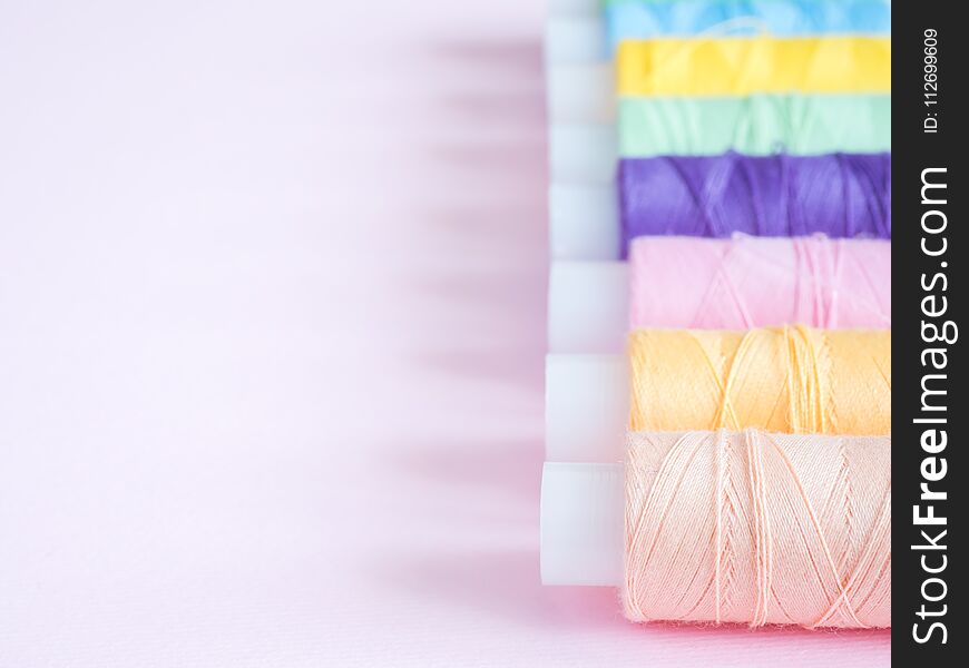 Colorful sewing buttons and thread on a pink background.