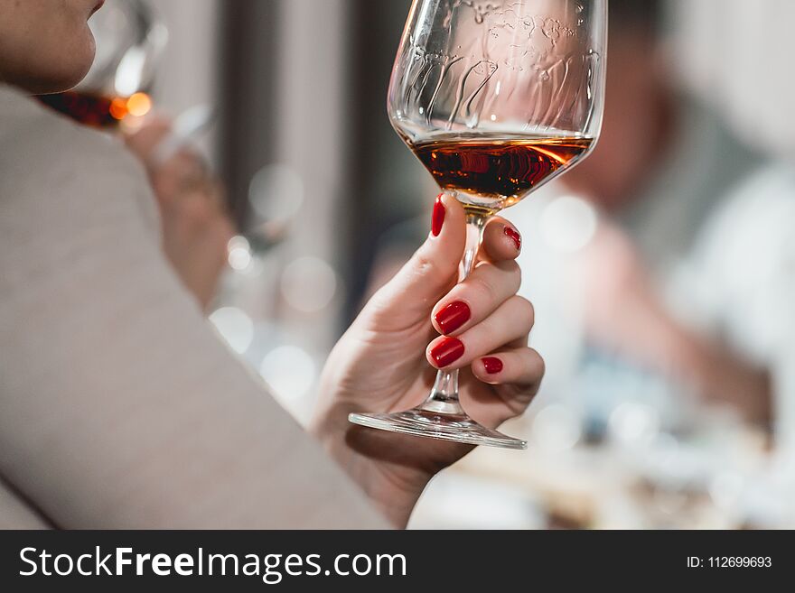 Woman holds glass of red wine. people consider the color of the wine and try how it smells in different glasses