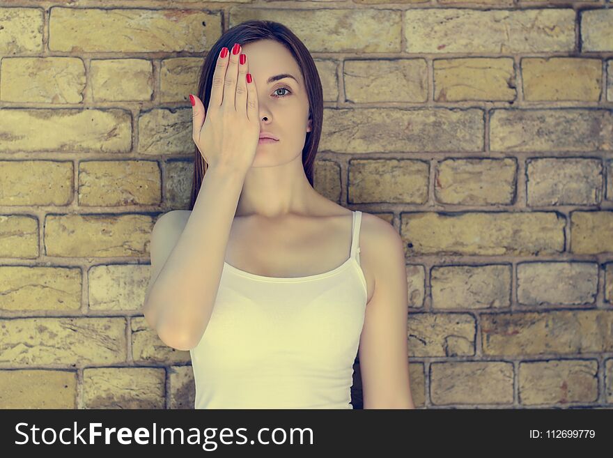 Portrait of young sad unhappy serious woman in white t-shirt closing half of her face . Brick wall on the background, vintage effect