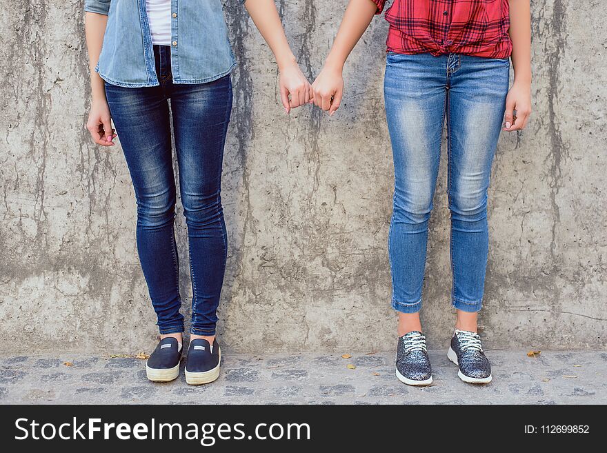 Help lesbians people comfort console concept. Close up photo of two cute lovely sweet teen age girls holding little fingers wearing stylish jeans isolated on concrete gray wall background